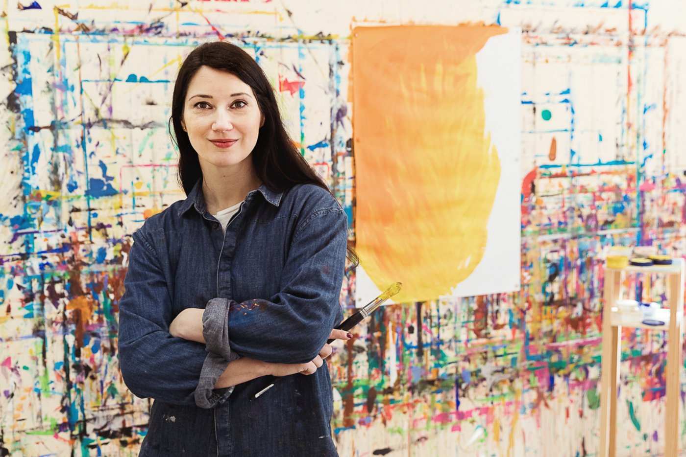 Malerin steht lächelnd in ihrem Atelier vor bemalter Wand, Portraitaufnahme