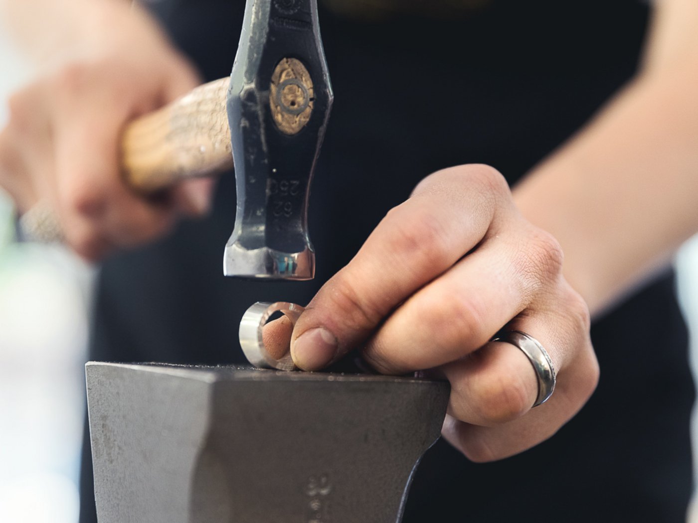 Goldschmied bearbeitet Ring mit Hammer auf Metallblock, Nahaufnahme