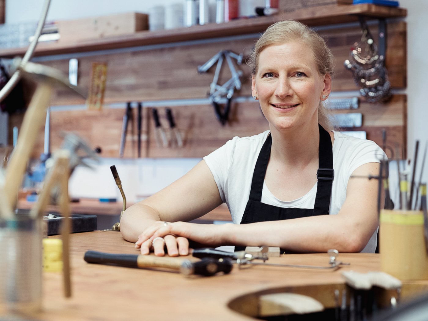 Goldschmiedin sitzt am Werktisch in Atelier, Portraitfoto 