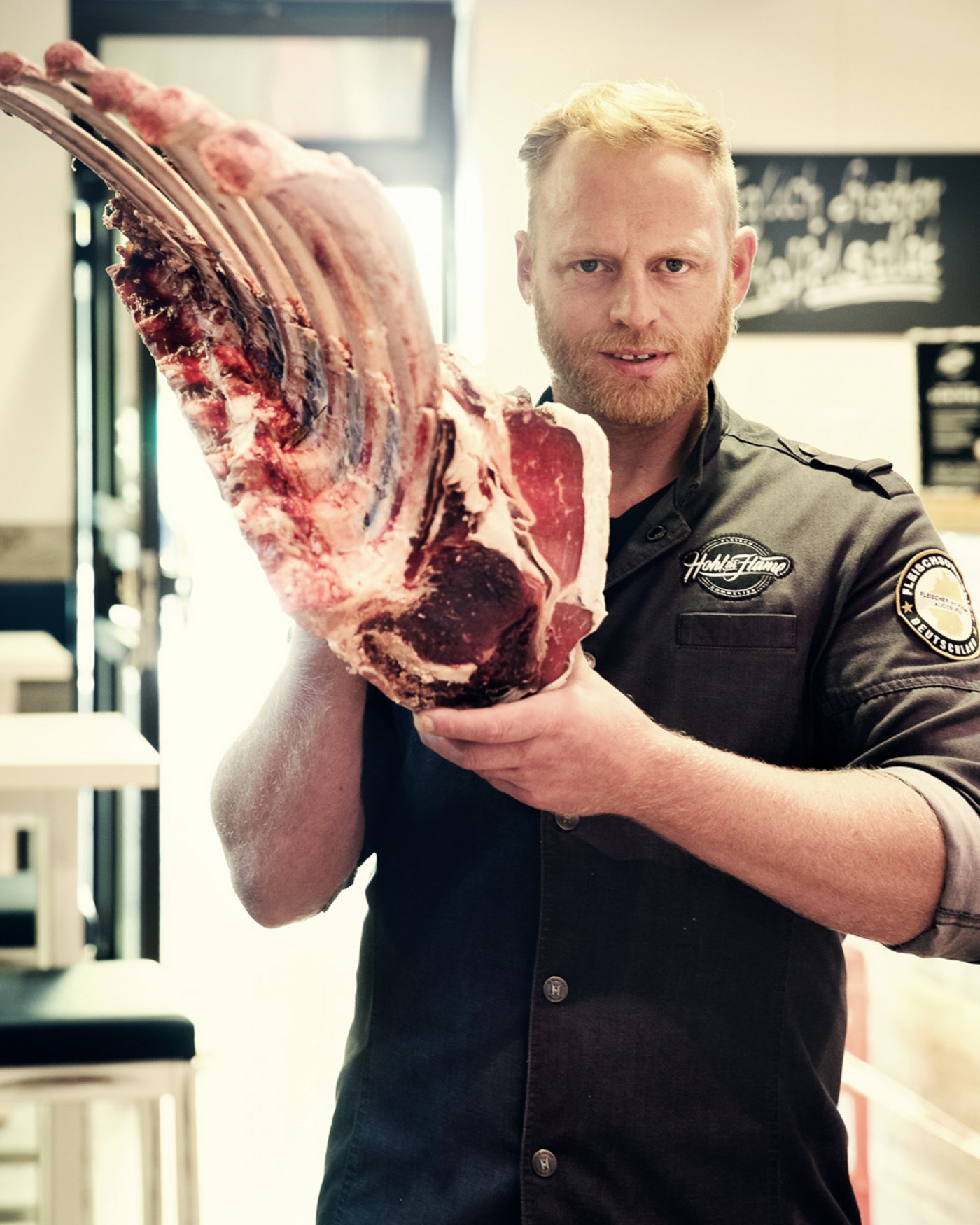 junger Metzger mit Bart hält ein großes Stück Fleisch in den Händen, Portrait