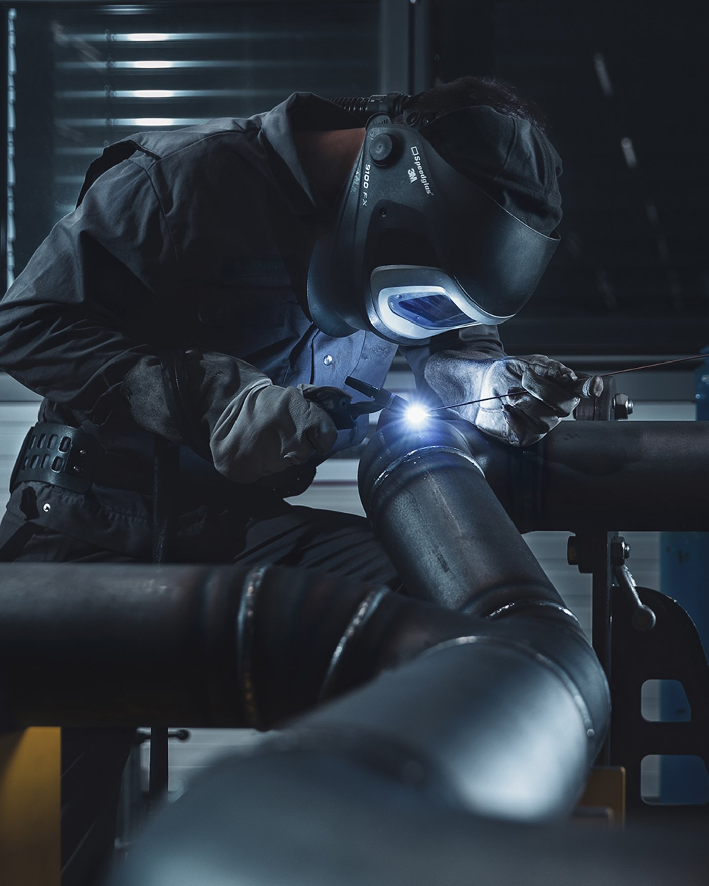 Industriearbeiter mit schwarzer Arbeitskleidung und Schutzbrille schweißt ein Rohr